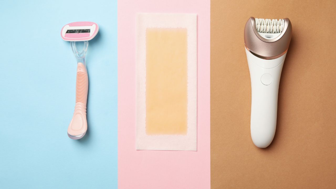 Razor, epilator, and wax strips on blue and pink background.