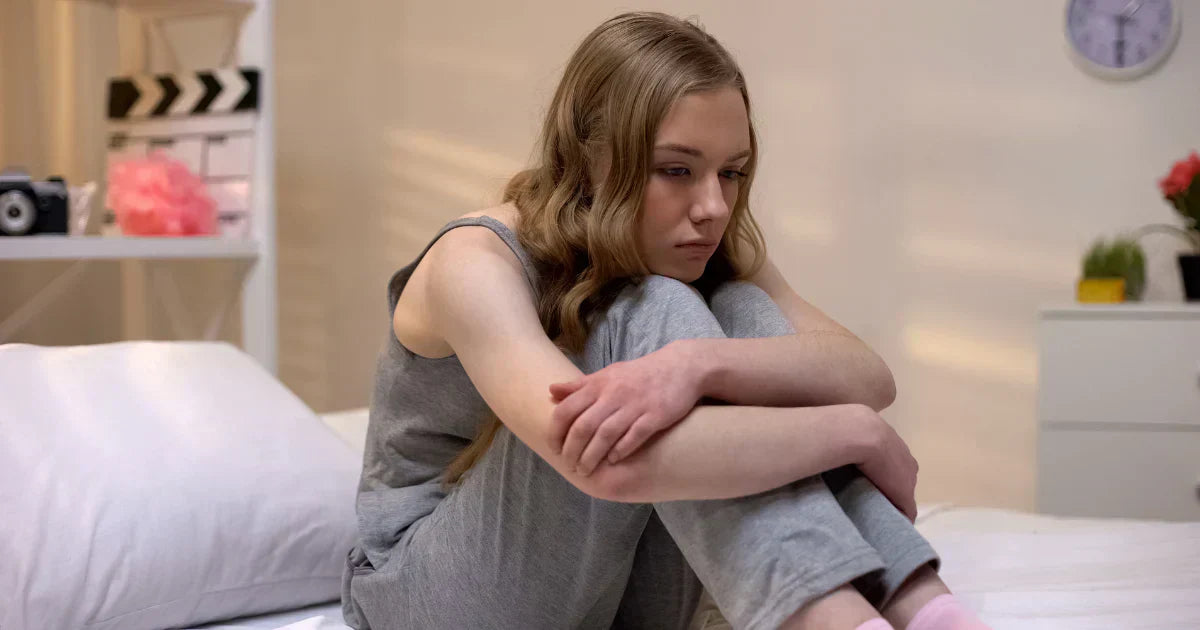 Image of an young teen sitting sadly on the bed
