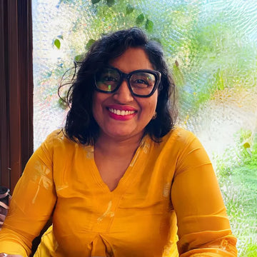 Woman wearing glasses and a yellow top in front of a textured window