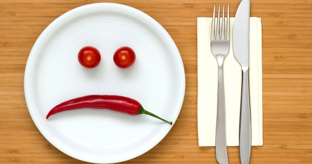 A sliced red bell pepper forms a smiley face on a plate. Two cherry tomatoes with black pupils serve as the eyes, with one winking playfully.