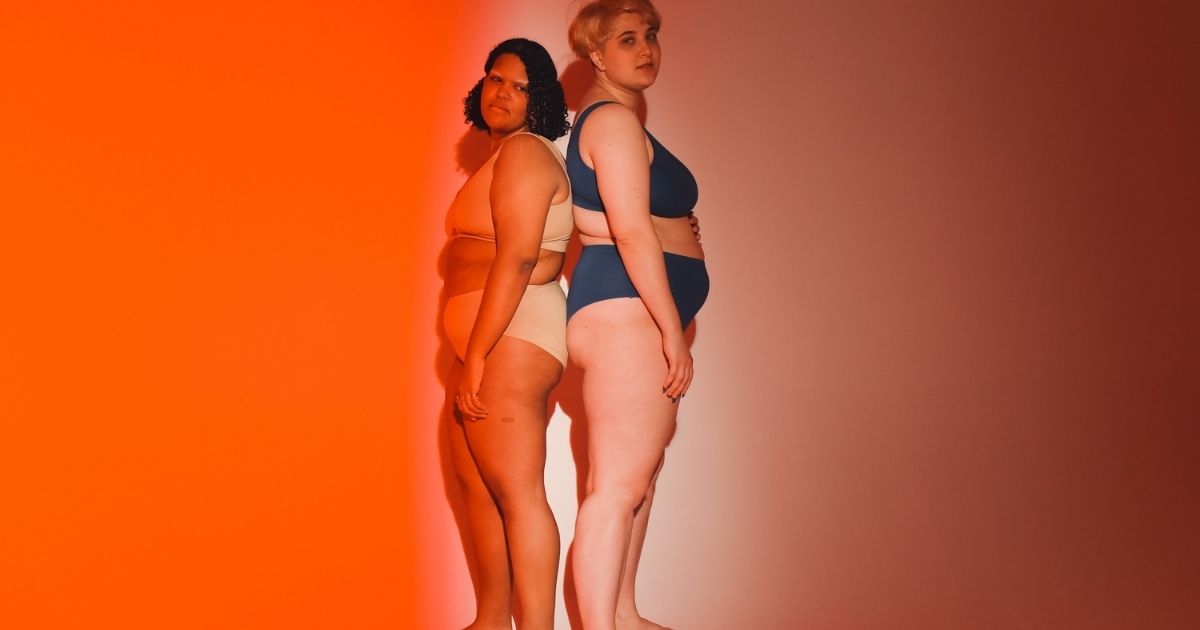 Two plus-size models are showcasing innerwear products in a photoshoot with a gradient background.