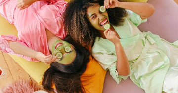 Two women smiling at camera while appling skincare.