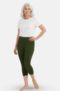 A woman modeling green capri leggings with a white t-shirt, standing against a light gray studio background.