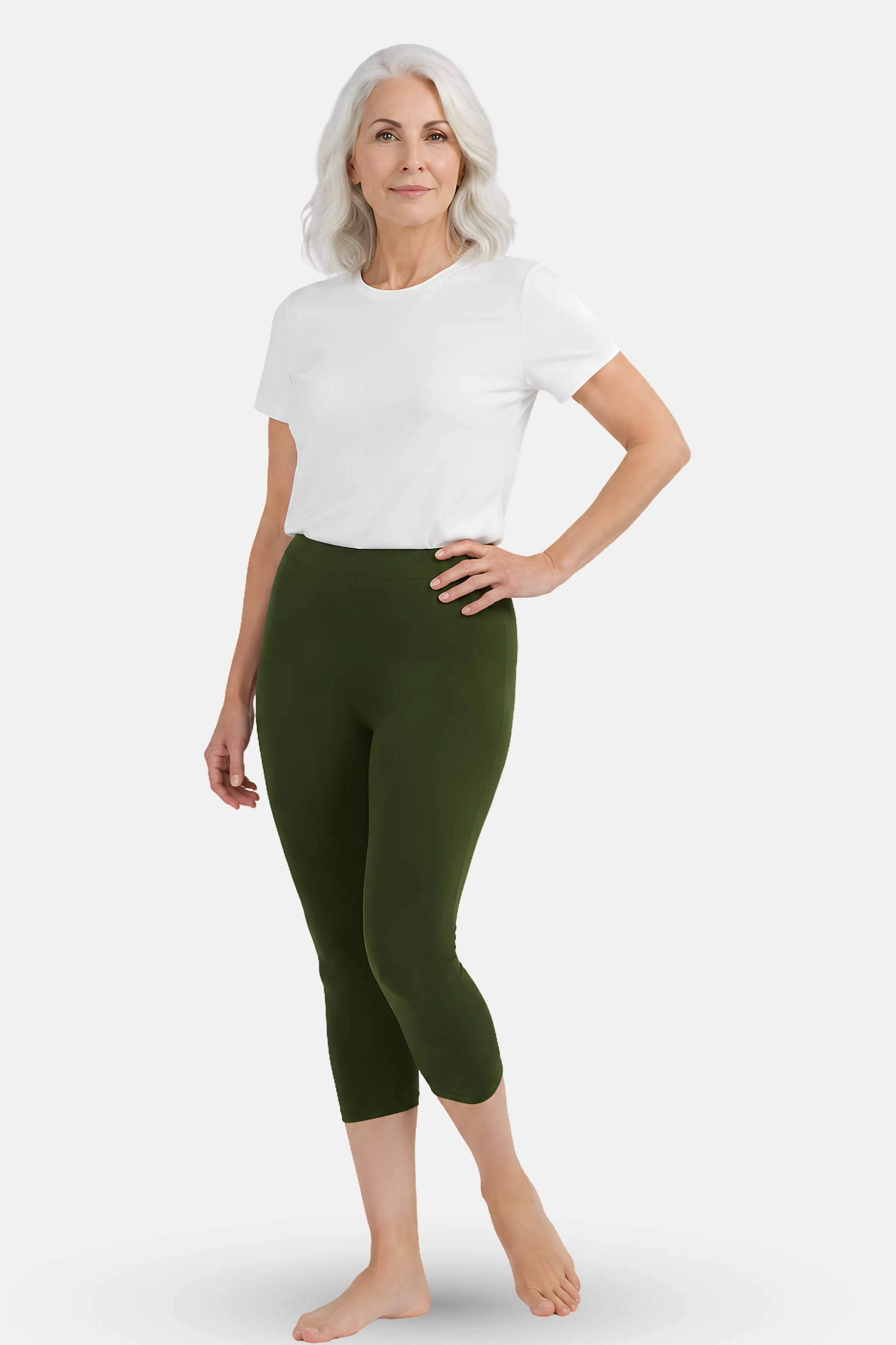 A woman modeling green capri leggings with a white t-shirt, standing against a light gray studio background.