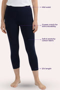 A model wearing dark navy capri leggings with text callouts pointing to features like mid waist, cusset crotch, stretchy fabric, and 3/4 length on a pale pink background.
