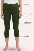 A model wearing green capri leggings with text callouts pointing to the mid-waist, cusset crotch, stretchy fabric, and 3/4 length on a pale pink background.