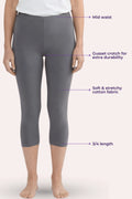A model wearing gray capri leggings with text callouts pointing to mid waist, gusset crotch, fabric, and 3/4 length on a pale pink background.