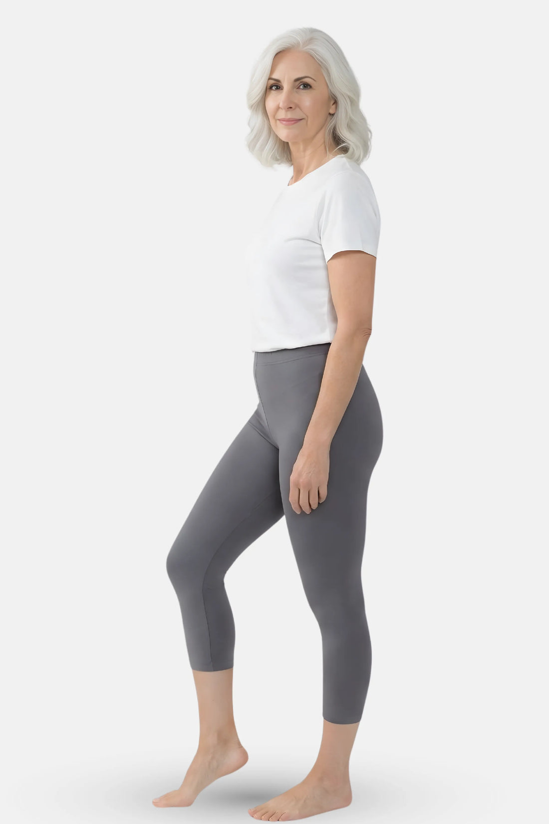 A woman wearing gray capri leggings and a white top against a light gray studio background.