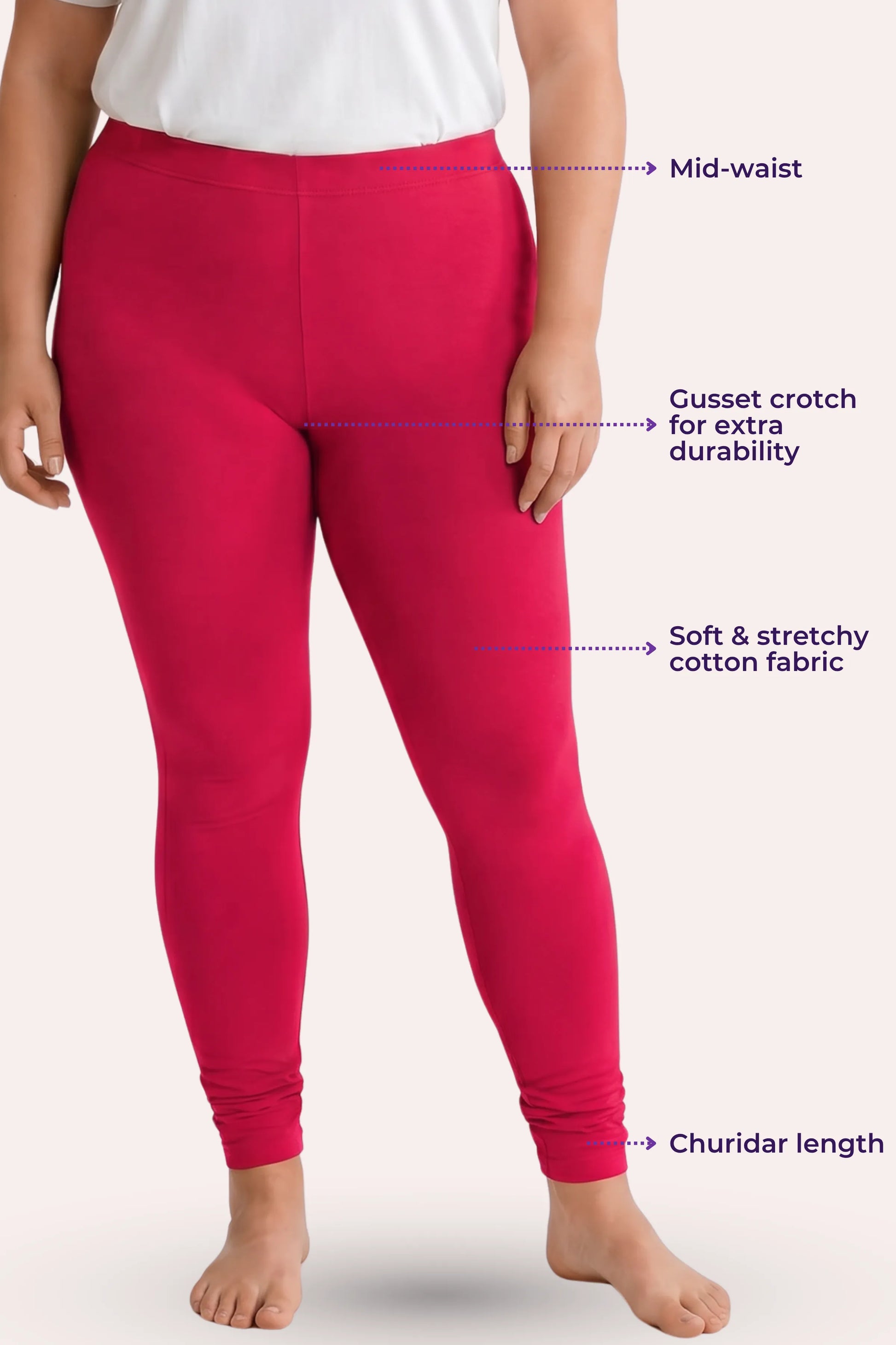 A model wearing dark pink leggings with overlaid callout labels pointing to the mid-waist, gusset crotch, stretchy fabric, and churidar hem on a pale background.