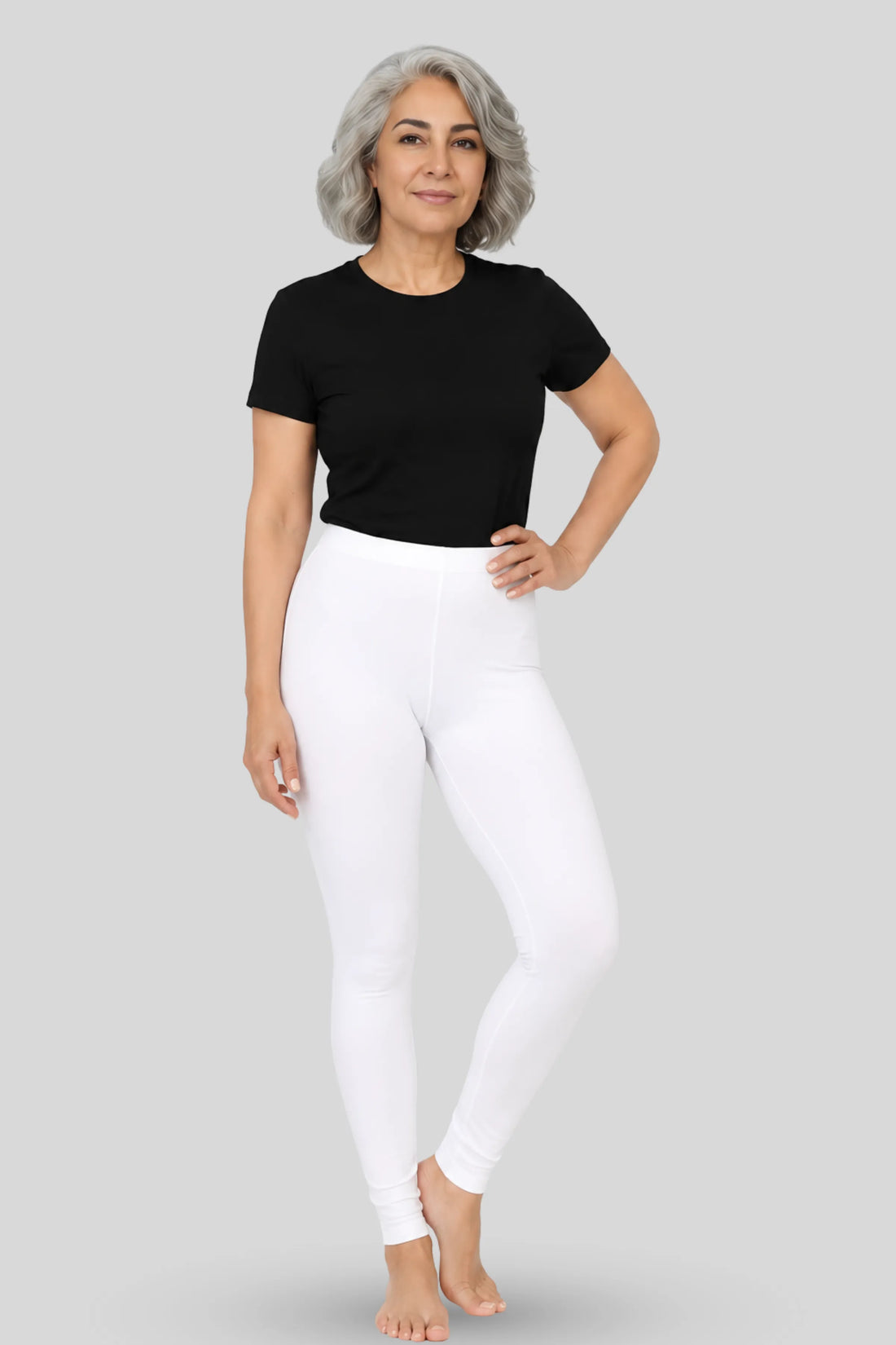 A woman modeling white mid-waisted leggings and a black short-sleeve t-shirt against a solid gray studio background.