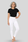 A woman modeling white mid-waisted leggings and a black short-sleeve t-shirt against a solid gray studio background.