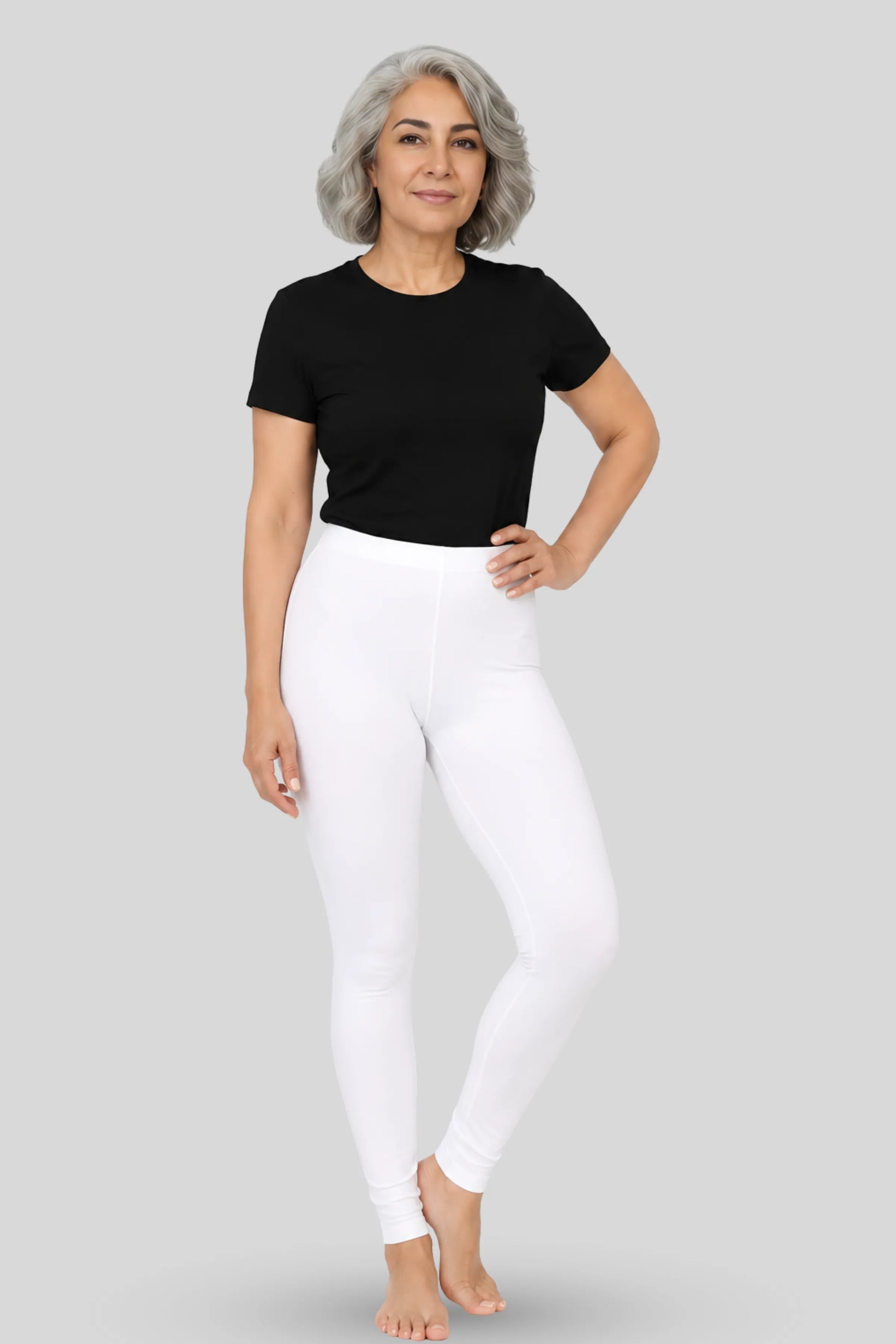 A woman modeling white mid-waisted leggings and a black short-sleeve t-shirt against a solid gray studio background.