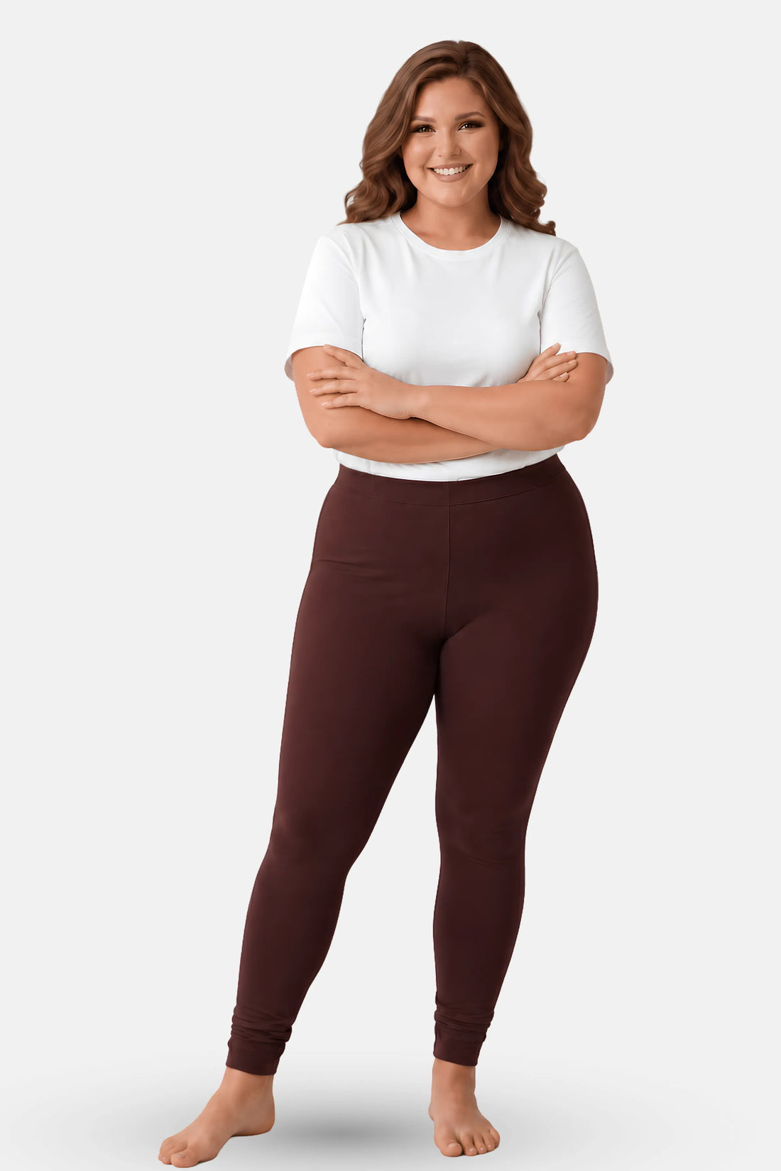 A woman modeling high-waisted, churidar leggings in a brown color, paired with a white t-shirt, against a solid light gray background.