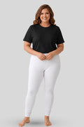 A woman modeling a black short t-shirt and white leggings against a solid light gray background.