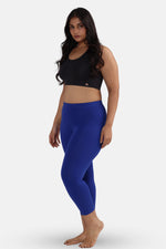 Woman wearing a black sports bra and blue leggings on a white background