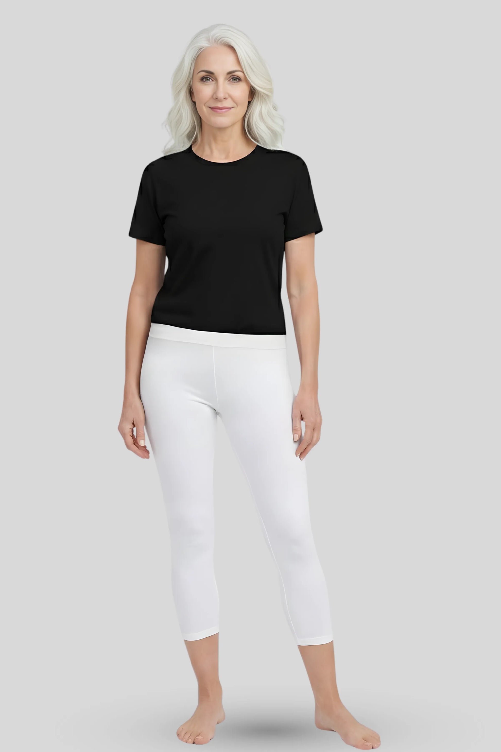 A woman modeling a black t-shirt and white cropped leggings against a solid light gray background.