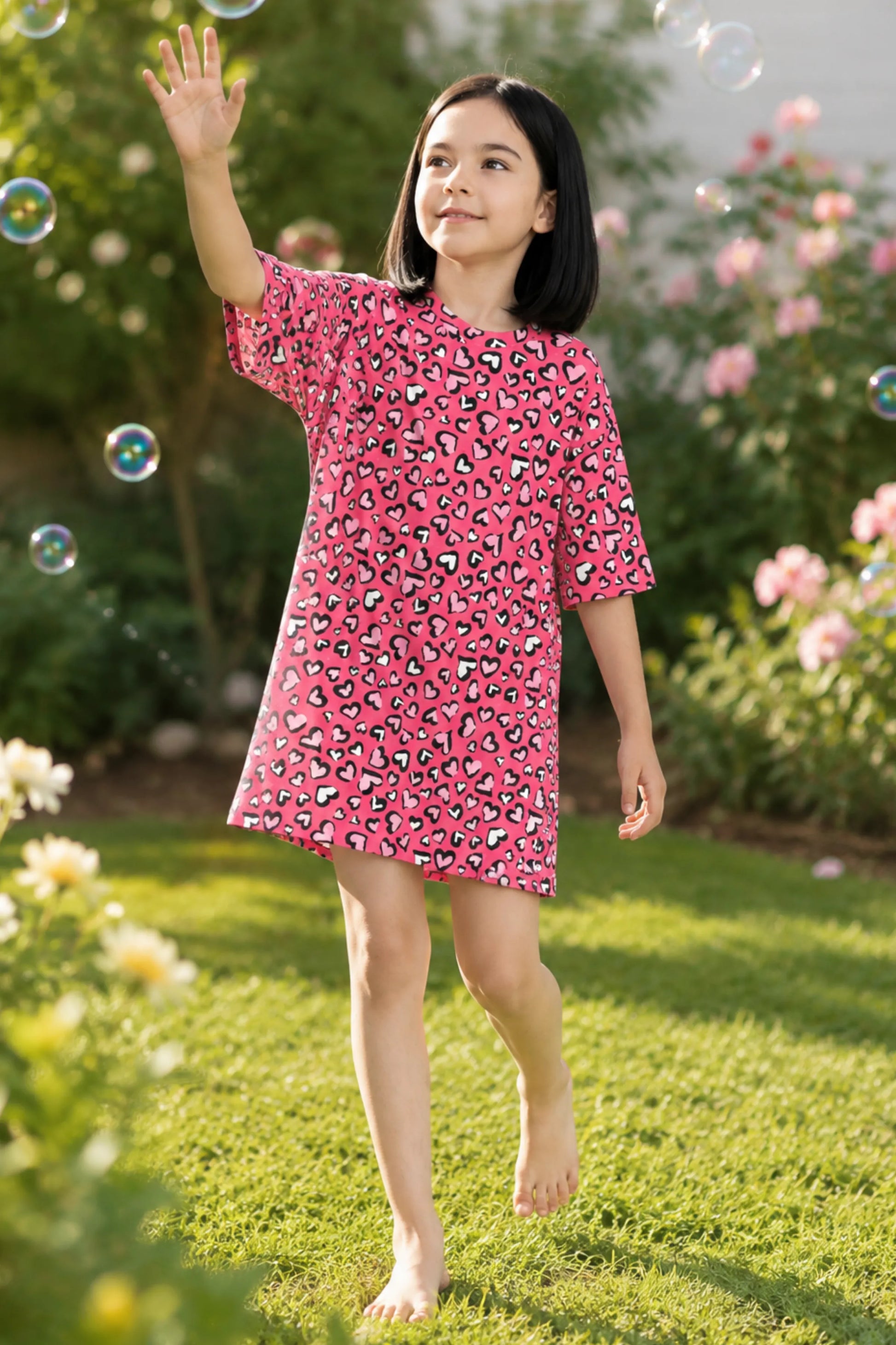 A young girl wearing a candy hearts t-shirt with a black, white, and gray abstract pattern. She is reaching up toward floating bubbles.