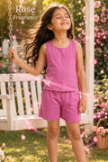 A young girl stands outdoors in a garden wearing a lavender sleeveless top and matching shorts. The image has a 'Rose' text overlay in the top left corner and purple magical swirl graphics on both sides.