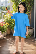 A girl wearing a oversized bright blue  dress. She is reaching toward a small orange butterfly on her finger.