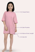 A girl model wearing a light pink dress with feature callouts to the closed neck, side pockets, above knee length, and side slit.