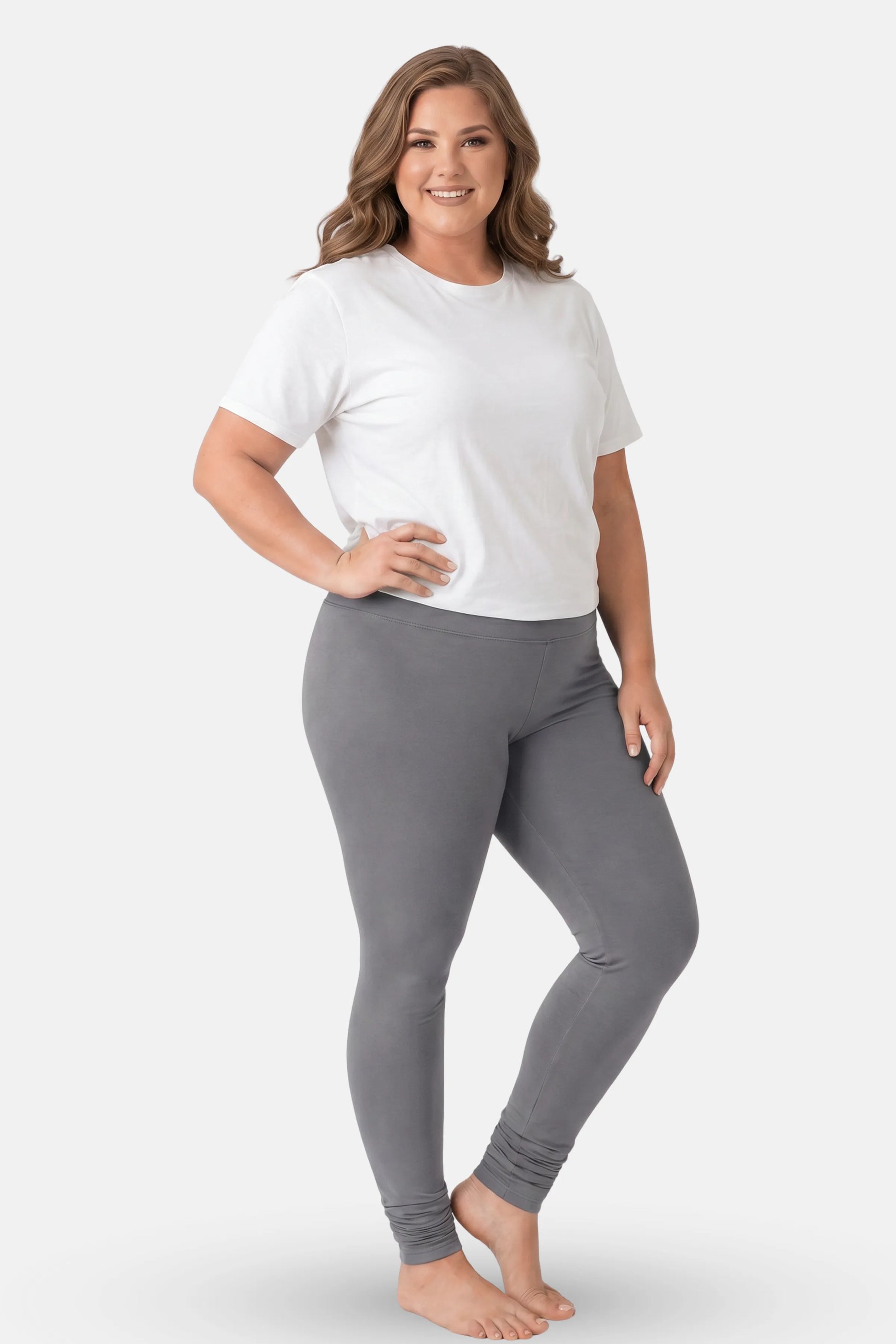 A woman modeling a white short t-shirt and gray high-waisted leggings against a light gray studio background.