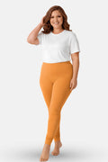 A woman modeling a white t-shirt and caramel leggings against a light gray studio background.