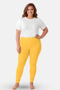 A woman modeling yellow leggings with a white t-shirt, standing against a light gray studio background.