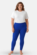 A woman modeling high-waisted, royal blue churidar leggings with a white t-shirt, standing against a light gray studio background.