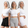Woman wearing a three different poses with white crop top and black, grey & white shorts on a white background