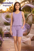 A young girl modeling a lavender sleeveless top and matching shorts set on a wooden deck, with decorative lavender sprigs and a hanging chair in the background. Text overlay reads 'Lavender Fragrance'.