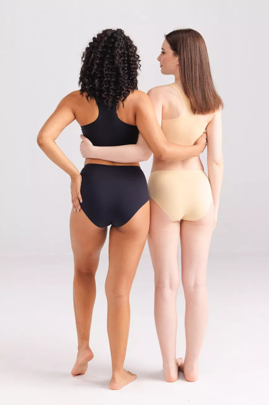 Two women wearing black and beige swimsuits standing back-to-back on a plain background