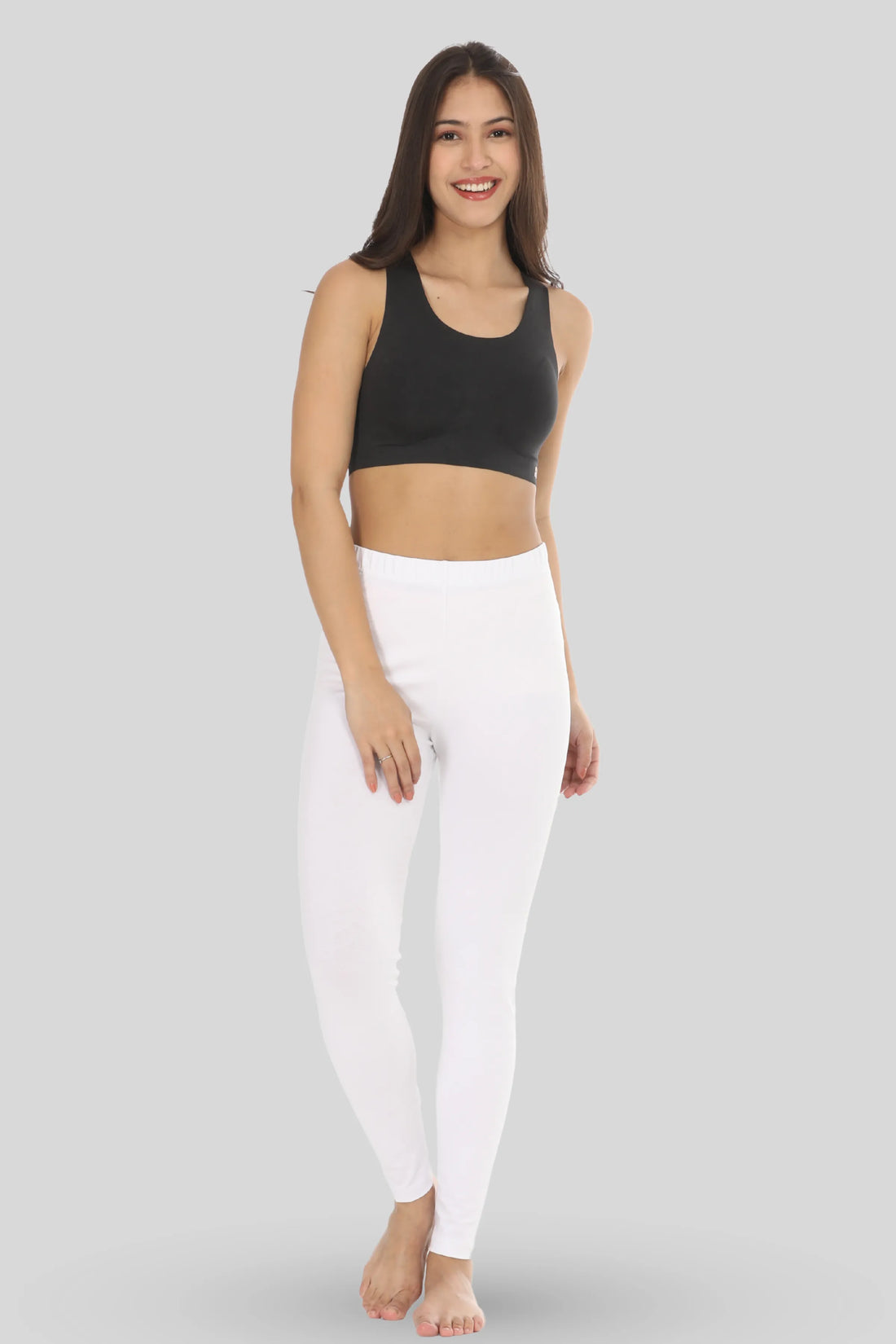 Woman wearing a black sports bra and white leggings on a white background